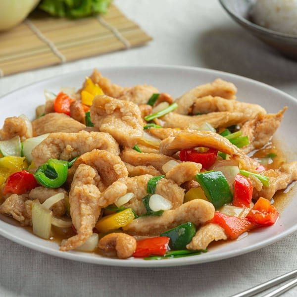 Burmese sweet and sour chicken with bell peppers and onions on a white plate.