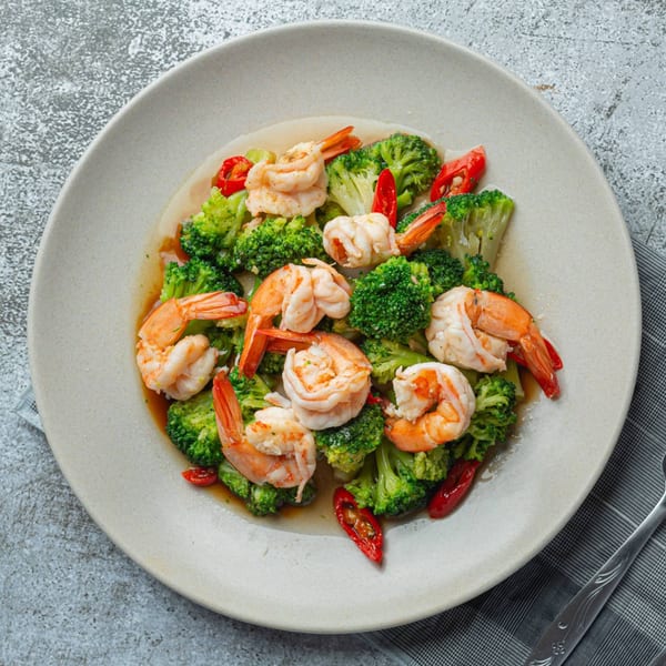 A Burmese dish of shrimp and broccoli florets with red chili slices on a light plate.