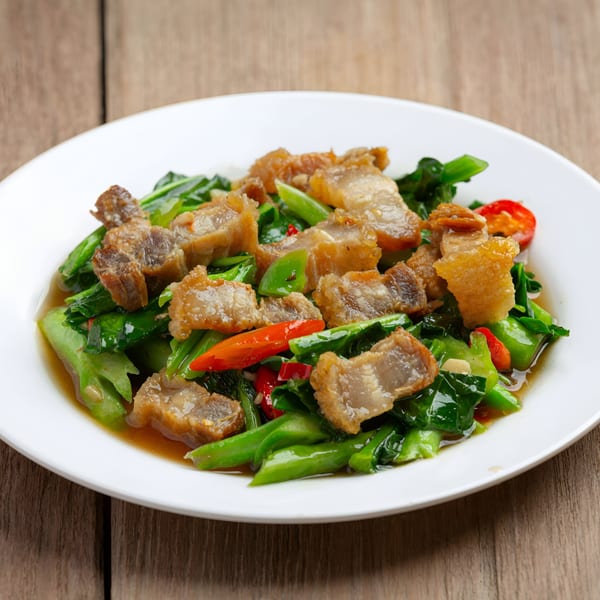 Burmese stir-fried crispy pork belly with green vegetables and red chilies on a white plate.